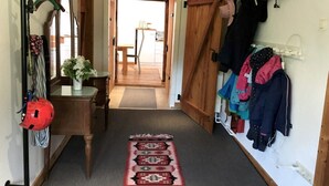 Un pasillo con una puerta de madera, un espejo, esquíes, un casco rojo y una alfombra.