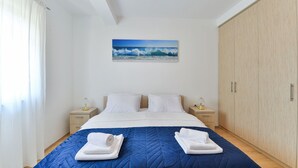 Una cama bien hecha con un edredón azul, dos almohadas blancas y dos toallas dobladas sobre la cama. Hay un cuadro de una ola en la pared sobre la cama.