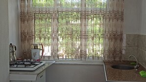 Une cuisine compacte équipée d’une cuisinière à gaz, d’un évier et d’une fenêtre agrémentée de rideaux décoratifs.