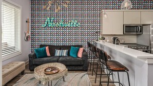 A modern living room with a black sofa, colorful cushions, a woven coffee table, and a patterned wall. - 1st Floor Condo No Steps - 2 miles to Downtown (Nashville)
