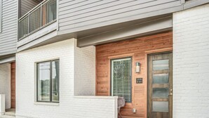 A modern two-story building with a white brick facade, a wooden front door with a glass panel, and a balcony with metal railings. - 1st Floor Condo No Steps - 2 miles to Downtown (Nashville)