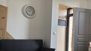 Ein modernes Wohnzimmer mit einem dunkelgrauen Sofa, einer Wanduhr und einer Tür, die auf einen Balkon führt.