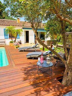 A wooden deck with lounge chairs, a small table with a bottle and glass, and a swimming pool. - Villa with private pool 🌿 3 bedrooms - near beaches & center - absolute calm (Cavalaire-sur-Mer)