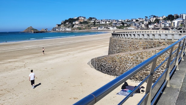 Une plage bordée d’un mur de pierres et d’une rambarde en métal.