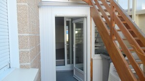 Un escalier étroit menant à une porte dotée d’un panneau de verre, situé à côté d’un mur blanc et d’une petite marche.