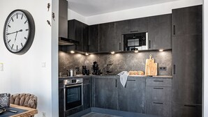Une cuisine moderne avec des meubles de couleur sombre, un four à micro-ondes et une grande horloge au mur.