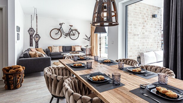 Un espace de restauration moderne avec une longue table en bois dressée pour un repas, entourée de fauteuils confortables.