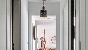 Un couloir mène à une salle à manger où l’on trouve un tapis noir, un plancher en bois et un luminaire suspendu.