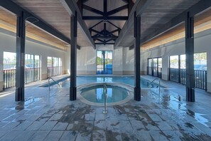 An indoor swimming pool with a central circular section and surrounding rectangular pools, surrounded by glass railings and a tiled floor.