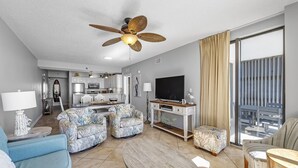 Een moderne woonkamer met een plafondventilator, een flatscreen televisie, een bank, een salontafel en een balkon met uitzicht.