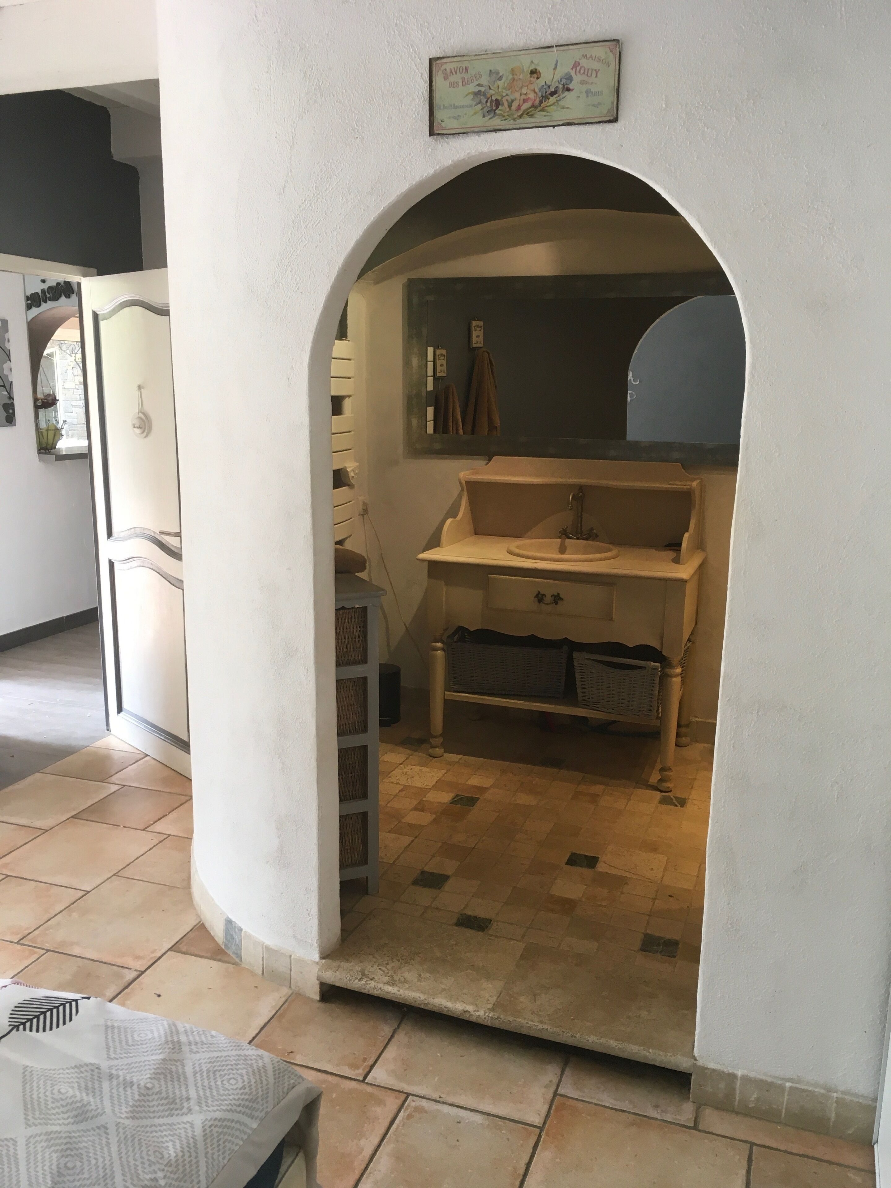 Un couloir étroit mène à une salle de bain équipée d’un lavabo et d’étagères.