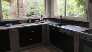 Moderni keittiö, jossa on sisäänrakennettu uuni, pesuallas ja ikkuna, josta avautuu näkymä puutarhaan.