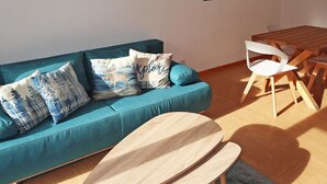 A living room with a teal sofa, wooden coffee table, white chairs, and a wooden dining table. - Ski-in/Ski-out Apartment with Pool (6 pers) - Les Orres 1800 (Les Orres)