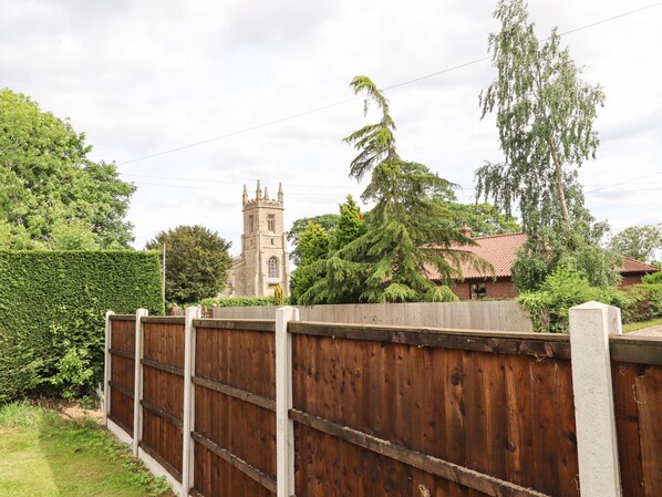 A church with a tall tower and a wooden fence in the foreground. - Honeybee Lodge (Woodhall Spa)