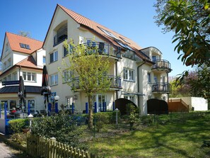 A multi-story building with balconies, a garden area, and a visible entrance.