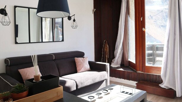 A modern living room with a dark sofa, a coffee table, and a large window with curtains.