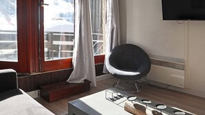 A modern room with a large window, a black chair, a flat-screen TV, and a wooden table with candles.