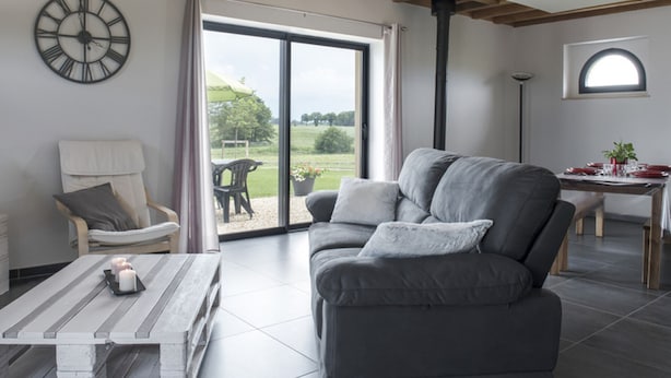 Un salon moderne avec un canapé gris, une table basse en bois et une grande fenêtre donnant sur un jardin.
