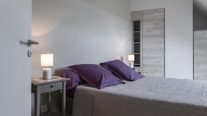 Une chambre à coucher avec un lit, deux tables de chevet avec des lampes, une armoire et une porte.