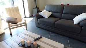 Un salon avec un canapé, un fauteuil, une table basse avec des bougies et une télécommande.