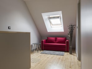 Un dormitorio estilo loft moderno con techo inclinado, tragaluz, un sofá rojo, una pequeña mesa redonda y un jarrón decorativo.