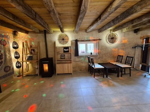 Un interior rústico con vigas de madera a la vista, una chimenea, una zona de comedor con sillas y un ventanal con cortinas.