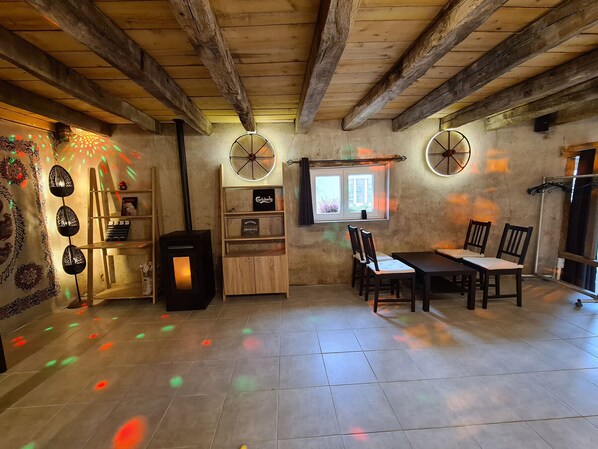 Un intérieur rustique avec des poutres apparentes, une cheminée, un coin repas avec des chaises et une fenêtre avec des rideaux.