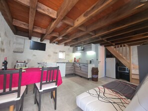 Una cocina acogedora con vigas de madera, una mesa de comedor con sillas, un sofá y un televisor colgado en la pared.