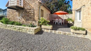 Un bâtiment en pierre doté d’un petit balcon, d’une cour en gravier et d’une table entourée de chaises, placée sous un parasol.
