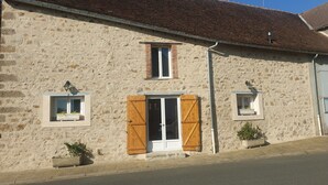 Un bâtiment en pierre avec un toit recouvert de tuiles, une porte en bois et deux petites fenêtres.