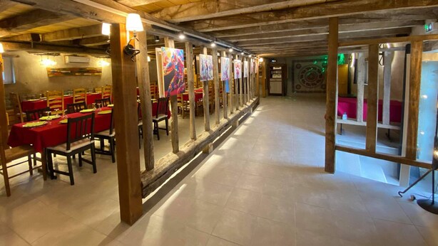 Un restaurant avec des poutres en bois, des tables et des chaises rouges, et des tableaux accrochés aux murs.