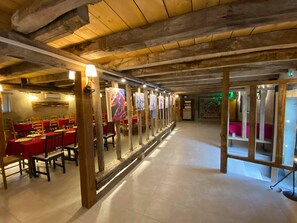 A restaurant with wooden beams, red tables, and chairs, and paintings on the walls.