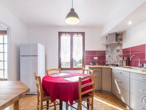 Une cuisine compacte comprenant un coin repas, un réfrigérateur, un crédence décorée et une fenêtre avec des rideaux.