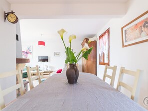 Une table à manger avec un vase de fleurs, des chaises, une horloge et un tableau encadré au mur.