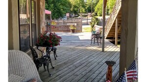 A wooden deck with outdoor furniture, a staircase, and a view of a road and trees. - Historic Stonehouse on Main St. Walking distance to shops, restaurant the River. (Hardy)