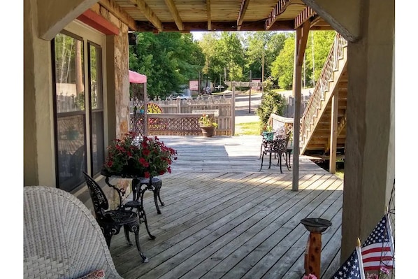 Une terrasse en bois avec des meubles d’extérieur, un escalier et une vue sur une route et des arbres.