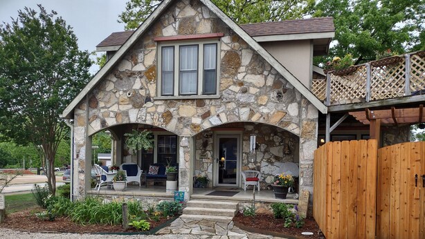 A stone house with a porch, a wooden fence, and a gravel driveway. - Historic Stonehouse on Main St. Walking distance to shops, restaurant the River. (Hardy)