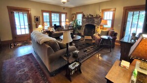 A spacious living room with a fireplace, comfortable seating, and a ceiling fan. - Historic Stonehouse on Main St. Walking distance to shops, restaurant the River. (Hardy)
