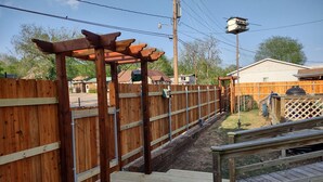 A wooden deck with a pergola structure, a wooden fence, and a small outdoor grill area. - Historic Stonehouse on Main St. Walking distance to shops, restaurant the River. (Hardy)