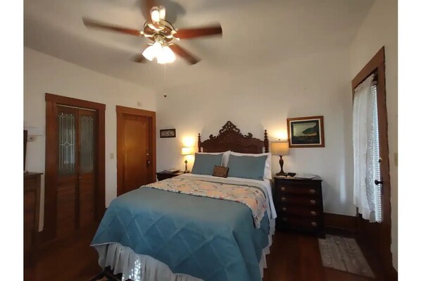 Une chambre à coucher comprenant un lit, une armoire en bois, un ventilateur de plafond et une table de chevet avec une lampe.