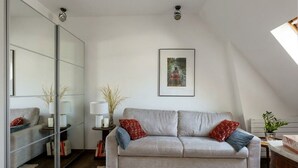 Un saló modern amb un sofà, una separació de vidre, un quadre al mur i una taula petita amb una làmpada.