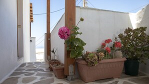 A narrow stone-paved pathway leading to a white building with multiple potted plants, including pink and orange flowers. - Cycladic Sea view Mansion near the Castle (Νάξος)