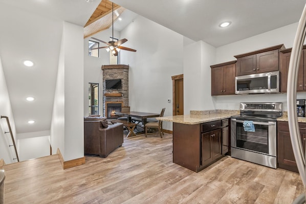 A spacious kitchen with a central island, wooden cabinets, a built-in oven, and a stone fireplace.
