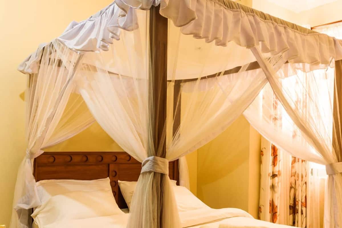 A four-poster canopy bed with a wooden headboard and a rolled towel on the bed.