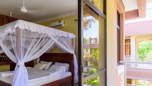 Een slaapkamer met een bed onder een klamboe, een balkon met een hekwerk, en uitzicht op groen buiten.