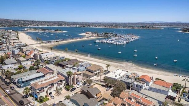 An aerial view of a coastal town with a marina, sandy beaches, and residential buildings.