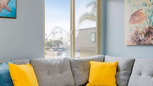 A living room with a grey sofa, yellow cushions, a starfish decoration, and a view of a building with a palm tree outside.