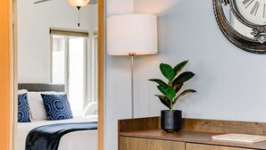 A hotel room with a bed, a bedside lamp, a potted plant, a wooden cabinet, and a wall clock.