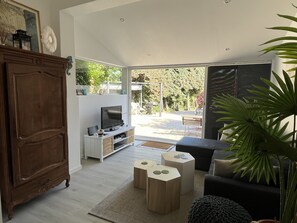 A modern living room with a wooden cabinet, a TV, and a sofa. There is a large window providing a view of the outdoors. - Renovated, air-conditioned house, 5 minutes from the beach (Saint-Cyr-sur-Mer)