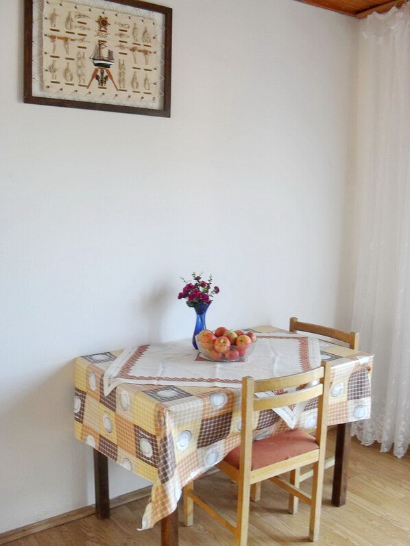 A small dining table with a checkered tablecloth, a vase with flowers, and a bowl of fruit.